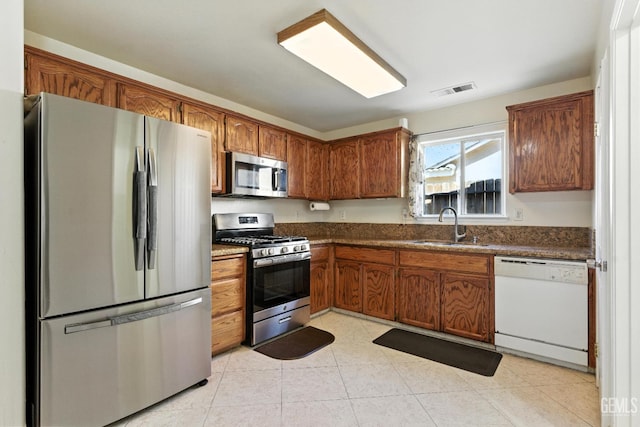 3023 Esperanza Dr, Bakersfield, CA 93313 - kitchen featuring stainless steel appliances, dark countertops, brown cabinets, and light tile patterned flooring