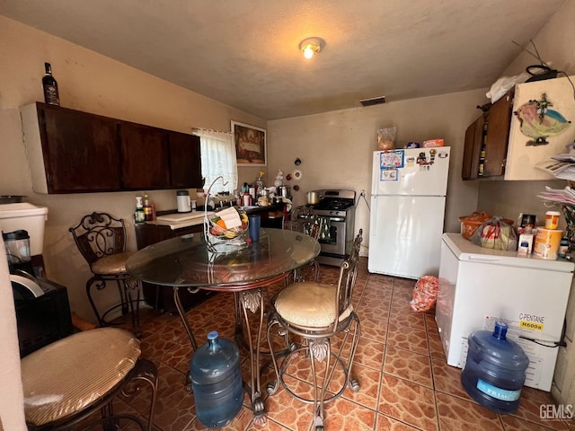 kitchen featuring refrigerator, dark tile patterned floors, white fridge, stainless steel gas range oven, and dark brown cabinets