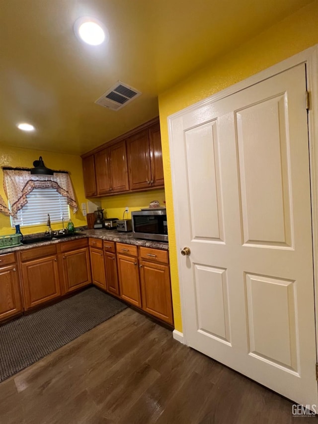 220 Tyler St, Taft, CA 93268 - kitchen with a sink, stainless steel microwave, dark wood-style floors, dark countertops, and brown cabinetry
