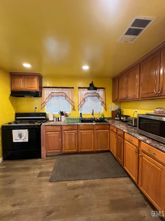 220 Tyler St, Taft, CA 93268 - kitchen with black gas range, stainless steel microwave, a sink, under cabinet range hood, and dark wood-style floors