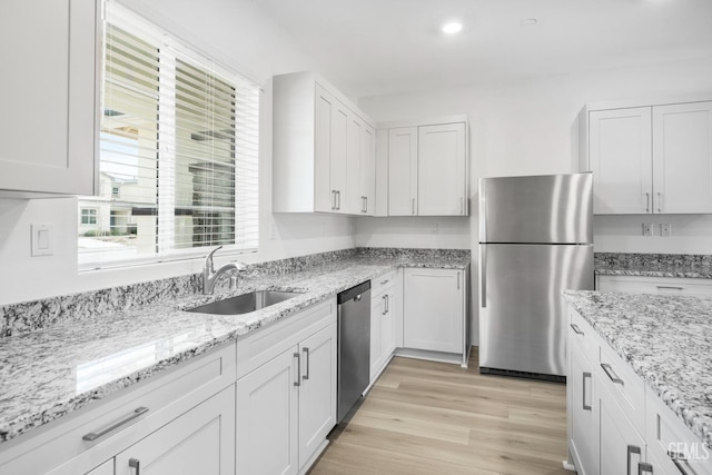 kitchen with sink, white cabinets, stainless steel appliances, light stone countertops, and light hardwood / wood-style flooring