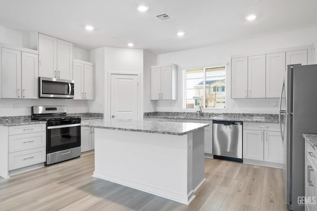 kitchen featuring stainless steel appliances, a center island, white cabinets, and light stone counters