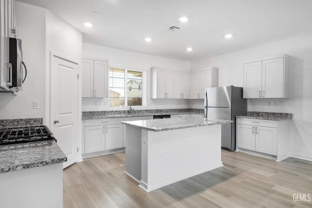 kitchen with white cabinetry, stainless steel appliances, a kitchen island, and light wood-type flooring