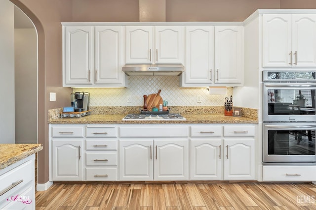 22 Emerald Isle Way, Bakersfield, CA 93314 - kitchen with white cabinets, arched walkways, white gas cooktop, stainless steel double oven, and under cabinet range hood