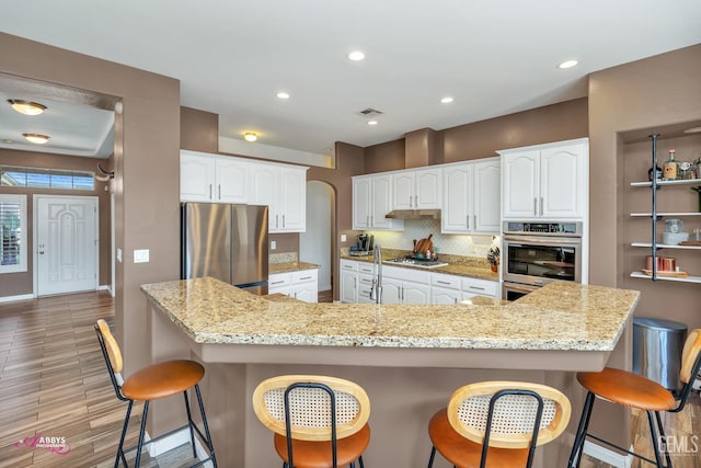 22 Emerald Isle Way, Bakersfield, CA 93314 - kitchen with a kitchen breakfast bar, light wood-type flooring, decorative backsplash, appliances with stainless steel finishes, and white cabinetry