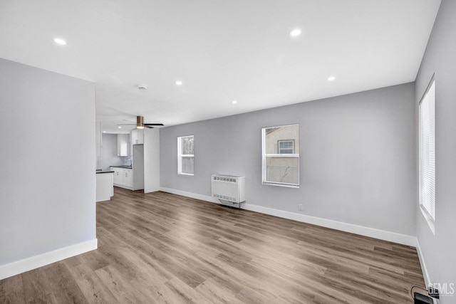 unfurnished living room with light wood-type flooring, heating unit, and ceiling fan