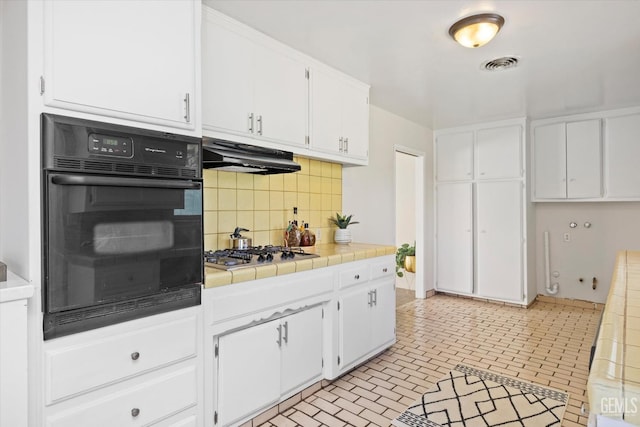 kitchen with stainless steel gas cooktop, white cabinetry, tile counters, oven, and backsplash