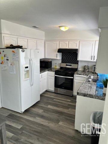 1024 Hazelnut St, Wasco, CA 93280 - kitchen featuring white fridge with ice dispenser, stainless steel gas range, under cabinet range hood, and white cabinets