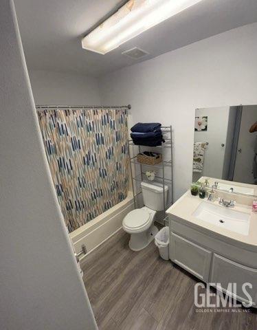 1024 Hazelnut St, Wasco, CA 93280 - bathroom featuring toilet, wood finished floors, shower / bathtub combination with curtain, and vanity