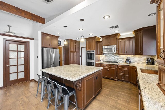 kitchen with beamed ceiling, backsplash, pendant lighting, a kitchen island, and appliances with stainless steel finishes