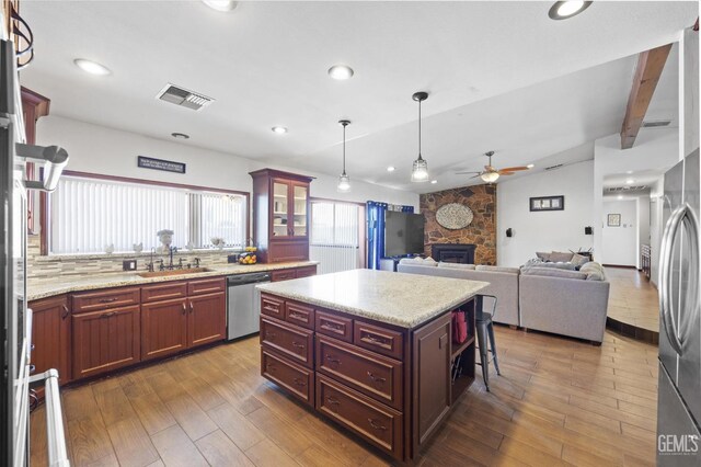 kitchen featuring ceiling fan, sink, stainless steel appliances, a fireplace, and a kitchen island