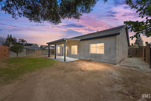 back of house at dusk featuring a fenced backyard, stucco siding, a lawn, and a patio