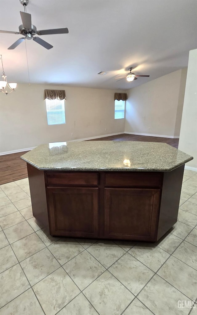 kitchen with ceiling fan, baseboards, a center island, and light stone countertops