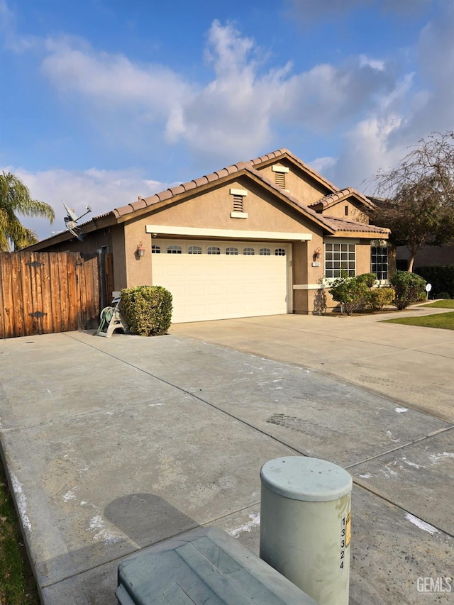 view of front of home featuring stucco siding, an attached garage, fence, driveway, and a tiled roof