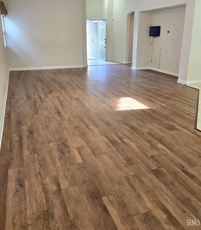 unfurnished living room featuring arched walkways, dark wood-type flooring, and baseboards