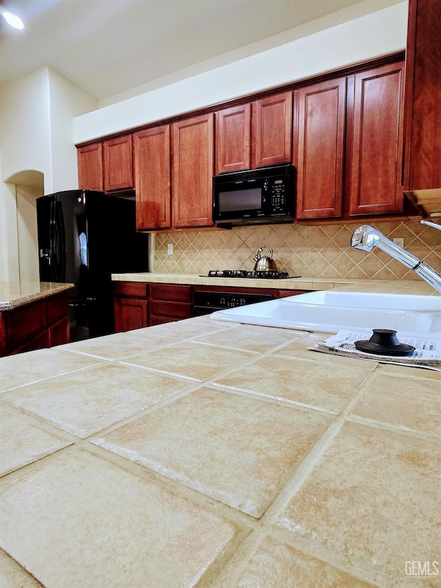 kitchen featuring light countertops, backsplash, and black appliances