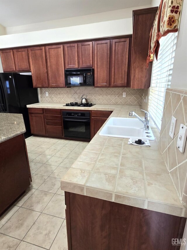 kitchen featuring decorative backsplash, a sink, black appliances, and light tile patterned floors