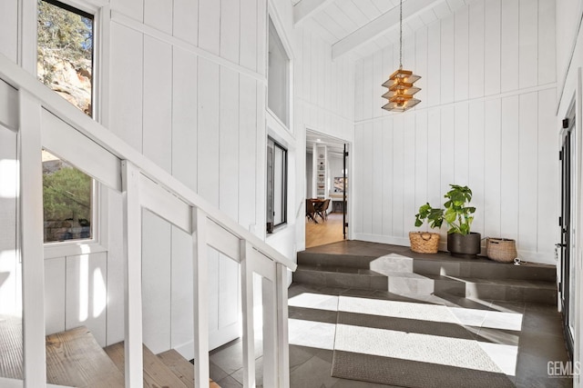 stairs with a healthy amount of sunlight, beamed ceiling, and a decorative wall