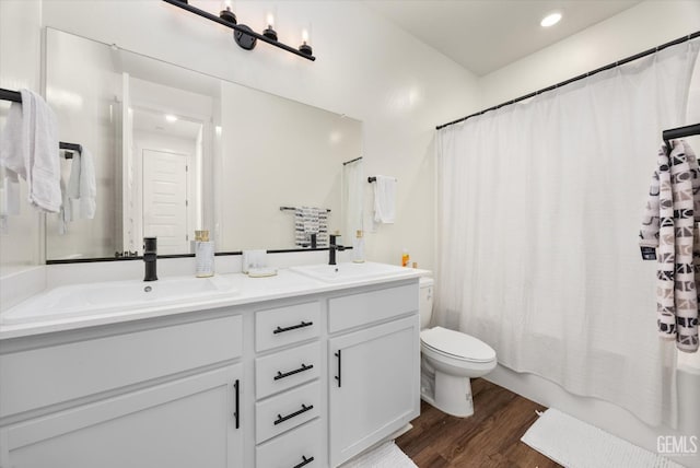 bathroom featuring double vanity, toilet, wood finished floors, and a sink