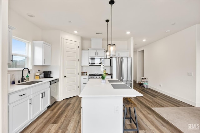 kitchen with visible vents, a center island, appliances with stainless steel finishes, wood finished floors, and a sink