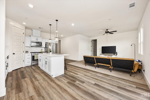 kitchen featuring visible vents, a kitchen bar, a kitchen island, white cabinetry, and appliances with stainless steel finishes