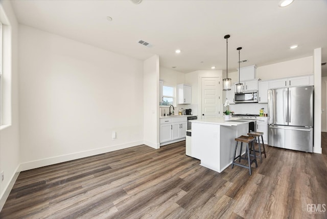 kitchen featuring visible vents, white cabinetry, stainless steel appliances, a kitchen bar, and a center island