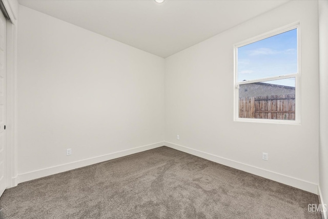 spare room featuring baseboards and dark carpet