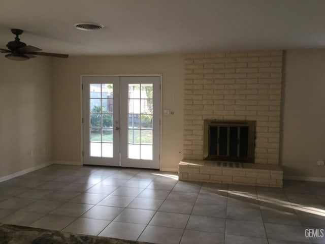 unfurnished living room with a brick fireplace, ceiling fan, french doors, and tile patterned flooring