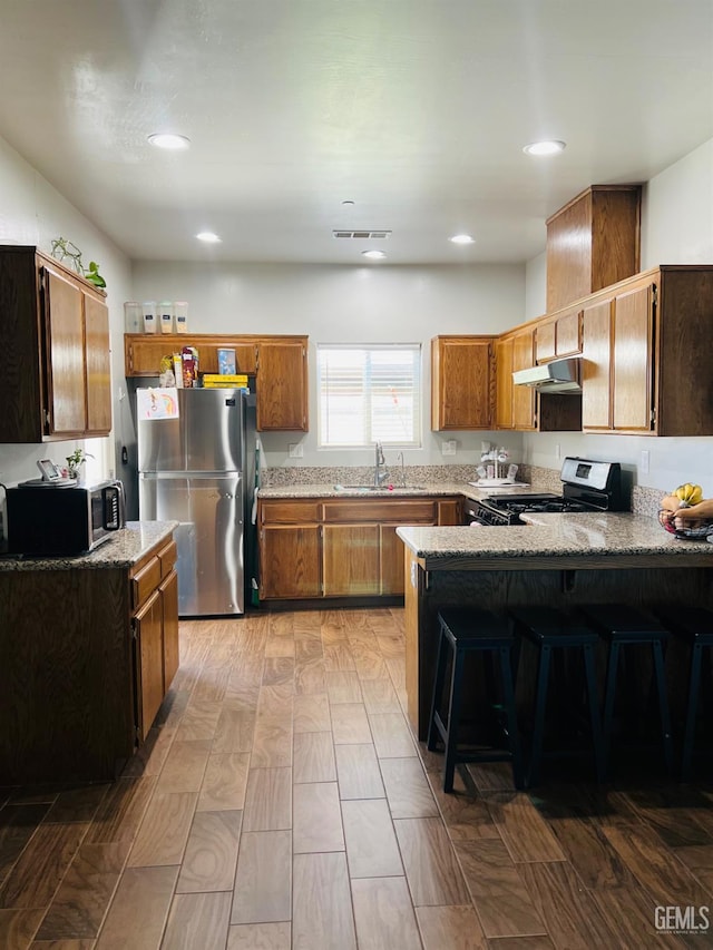 318 Smoke Tree Ct, Wasco, CA 93280 - kitchen featuring stainless steel appliances, a sink, under cabinet range hood, a peninsula, and light stone countertops