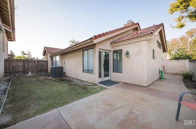 rear view of property with central AC unit, a lawn, and a patio