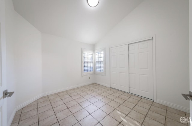 unfurnished bedroom with light tile patterned floors, vaulted ceiling, and a closet