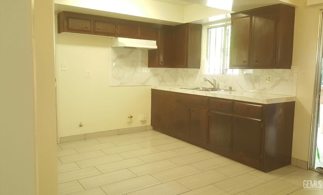 kitchen with baseboards, tile counters, decorative backsplash, under cabinet range hood, and a sink