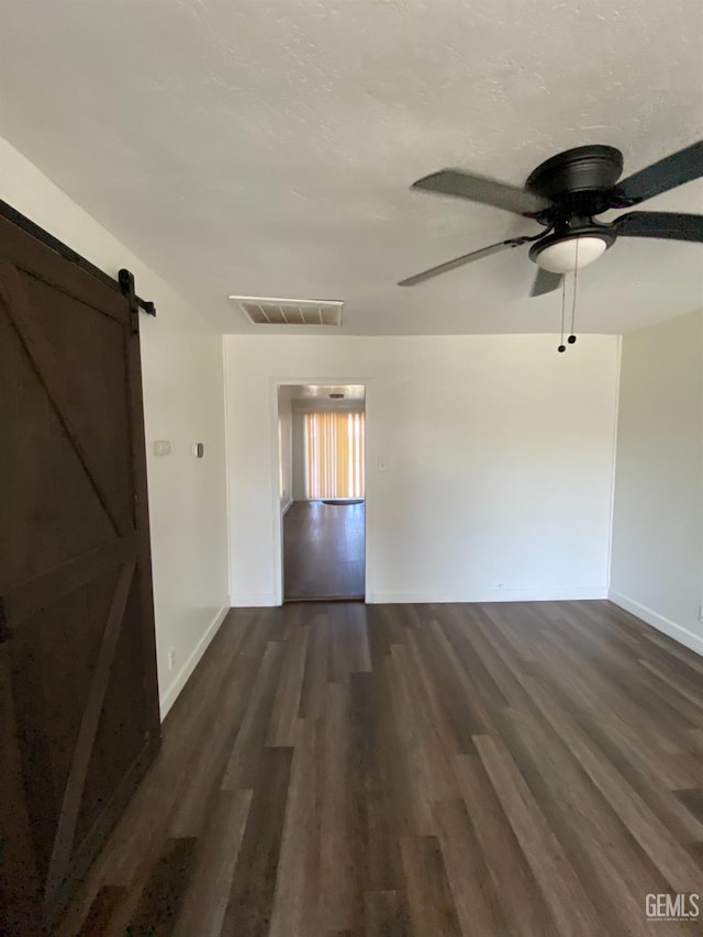 unfurnished room with dark hardwood / wood-style floors, ceiling fan, and a barn door