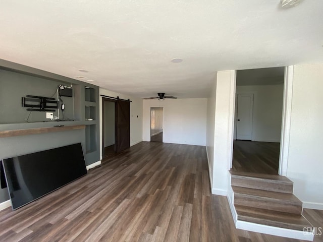 unfurnished living room with a barn door, ceiling fan, and dark wood-type flooring