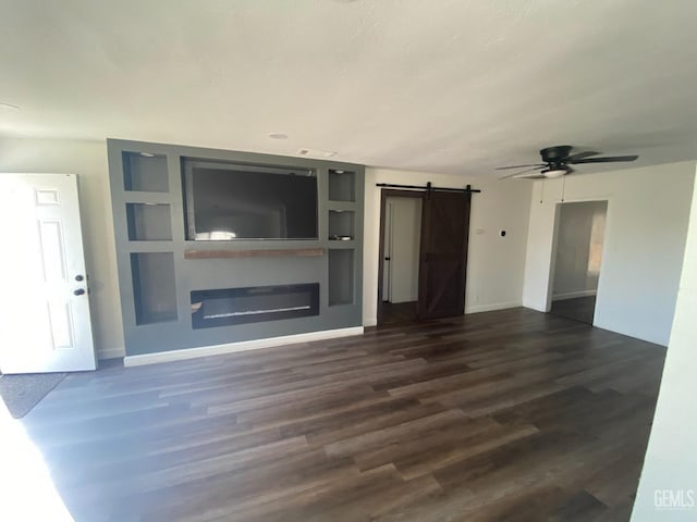 unfurnished living room featuring a barn door, dark hardwood / wood-style floors, built in features, and ceiling fan