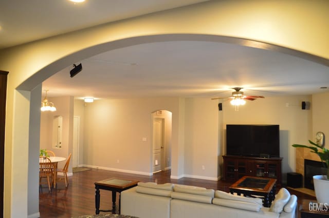 living area with baseboards, arched walkways, dark wood finished floors, and ceiling fan with notable chandelier