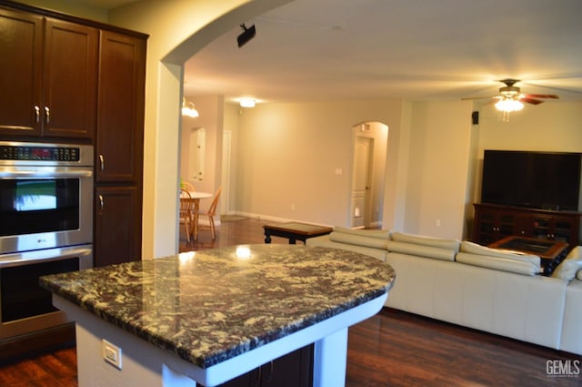 kitchen featuring arched walkways, a kitchen island, open floor plan, dark wood-style flooring, and double oven