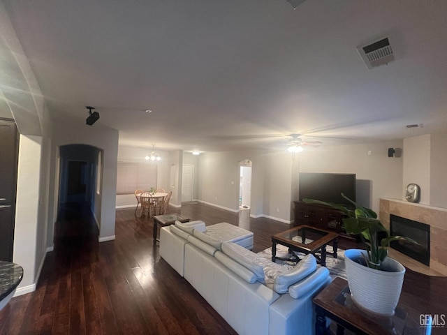 living room featuring arched walkways, visible vents, a tiled fireplace, wood finished floors, and baseboards