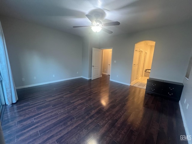 unfurnished bedroom featuring baseboards, arched walkways, and dark wood-style flooring