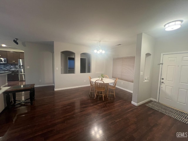 dining space with arched walkways, a notable chandelier, dark wood finished floors, and baseboards