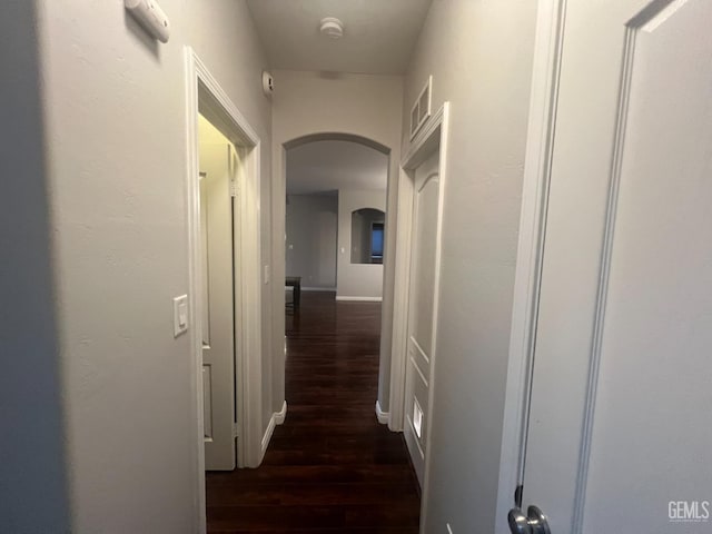 corridor with dark wood-style floors, baseboards, visible vents, and arched walkways