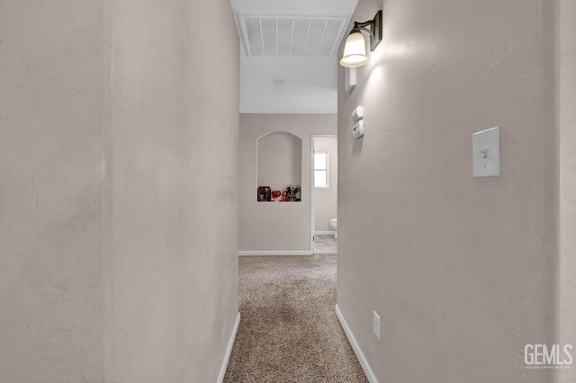 hallway with carpet floors, baseboards, visible vents, and a textured wall