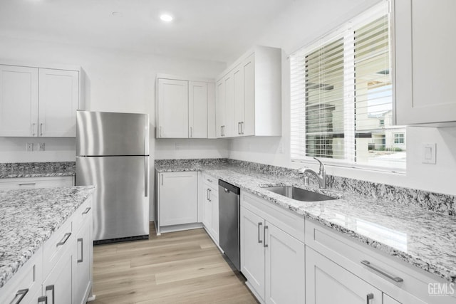 kitchen with white cabinets, light wood-style flooring, light stone counters, appliances with stainless steel finishes, and a sink