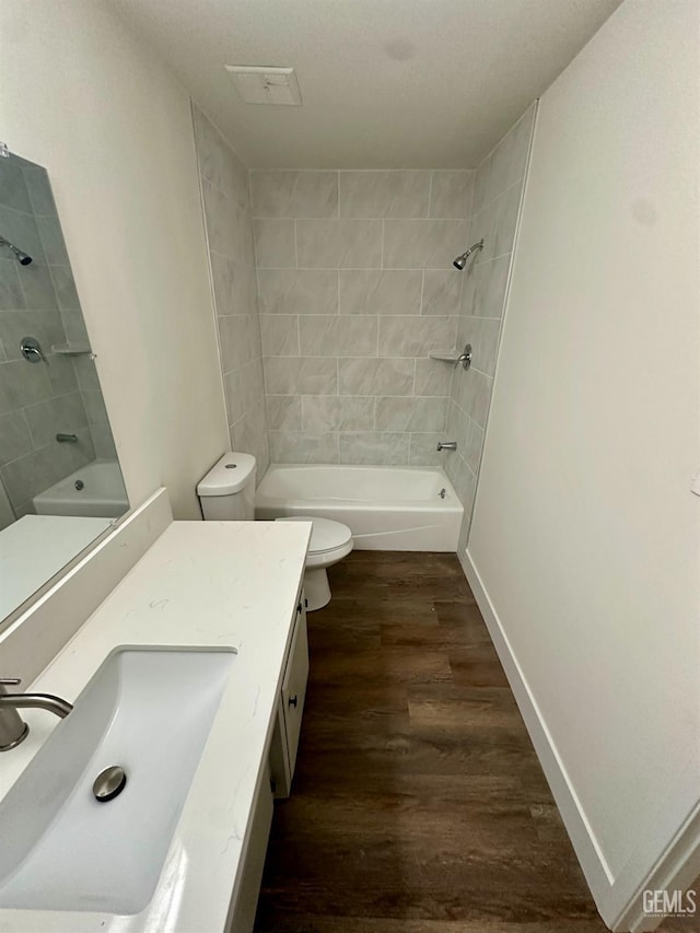 full bathroom featuring hardwood / wood-style flooring, vanity, tiled shower / bath combo, and toilet