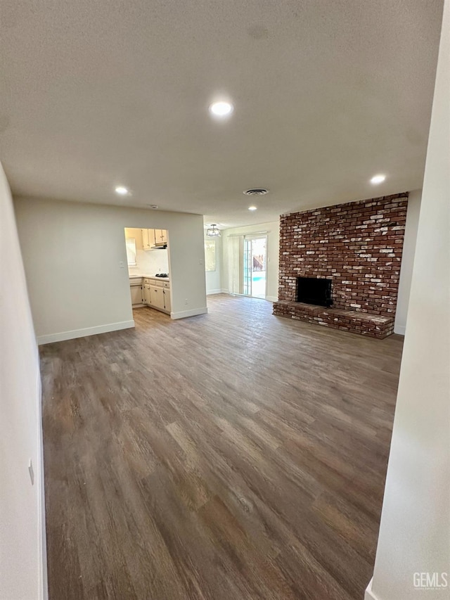 unfurnished living room with dark hardwood / wood-style floors, a brick fireplace, and a textured ceiling