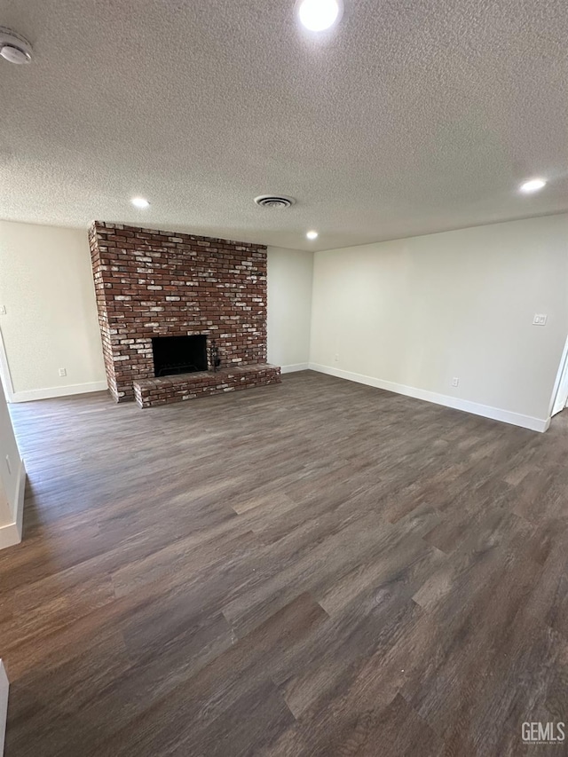 unfurnished living room with dark hardwood / wood-style flooring, a brick fireplace, and a textured ceiling