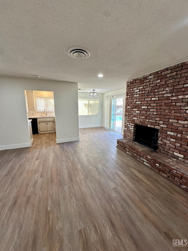 unfurnished living room with light hardwood / wood-style floors, a brick fireplace, and a textured ceiling