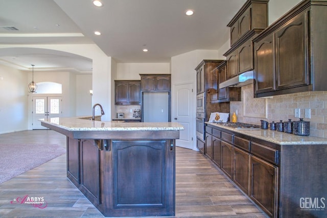 kitchen with hardwood / wood-style floors, dark brown cabinets, stainless steel appliances, and an island with sink