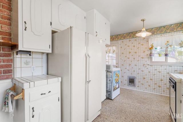 kitchen featuring heating unit, freestanding refrigerator, decorative light fixtures, white cabinetry, and tile countertops