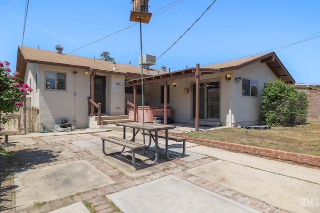 rear view of property with stucco siding, fence, a patio area, and a hot tub
